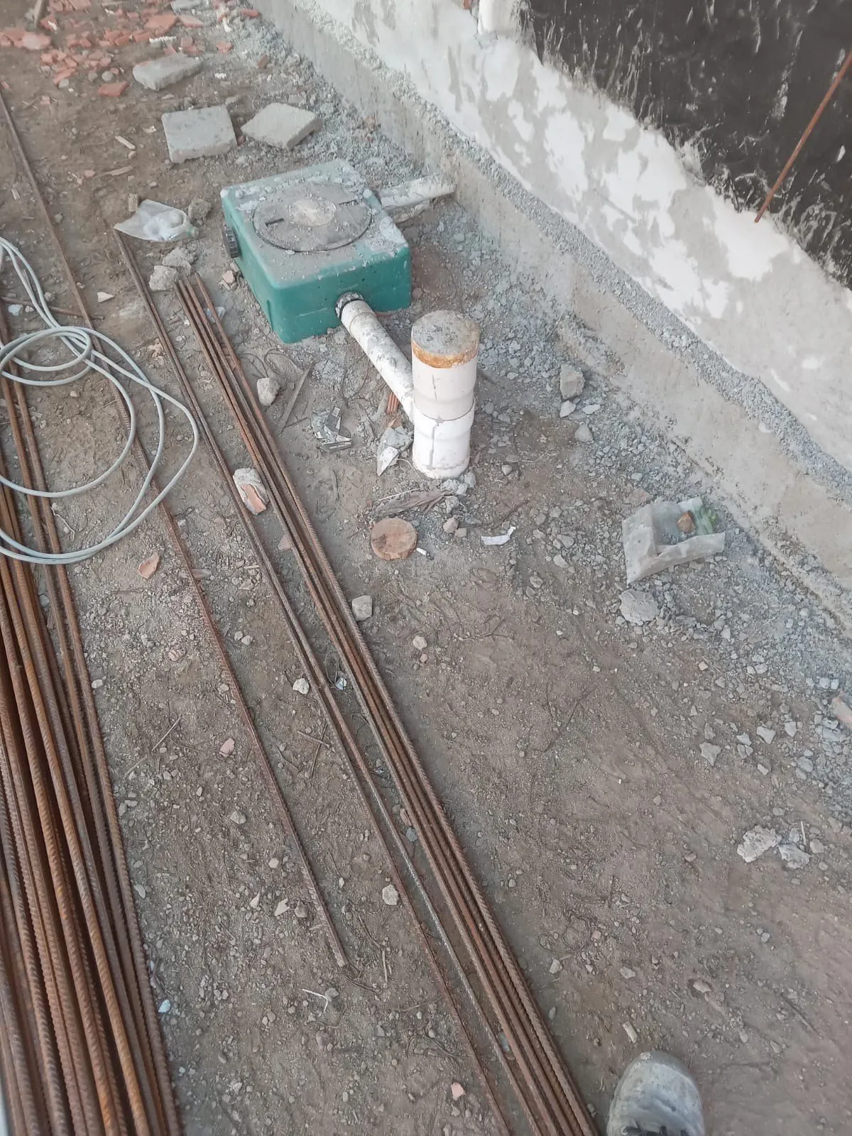 Arqueta, tubo de desagüe y varillas de acero junto a un muro, antes de hacer la solera