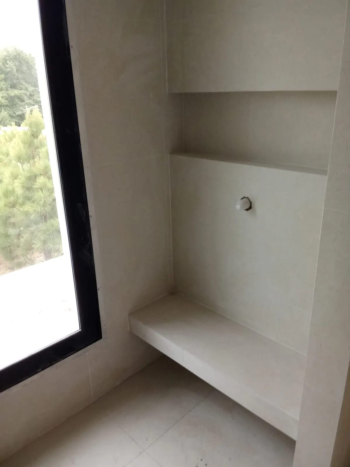 Baño con banco de obra y hornacinas en porcelánico claro, junto a una ventana