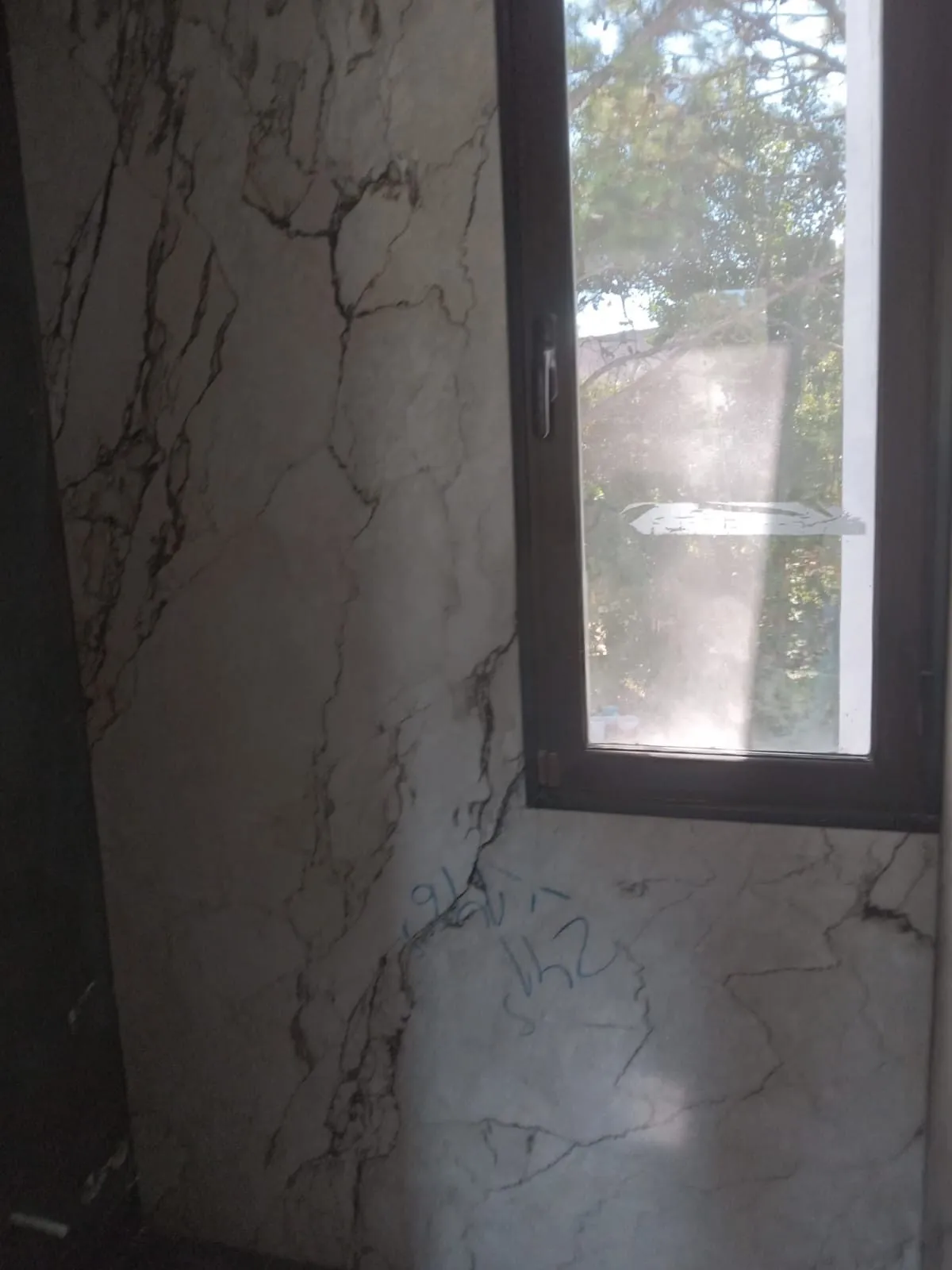 Pared de baño revestida de porcelánico efecto mármol junto a una ventana
