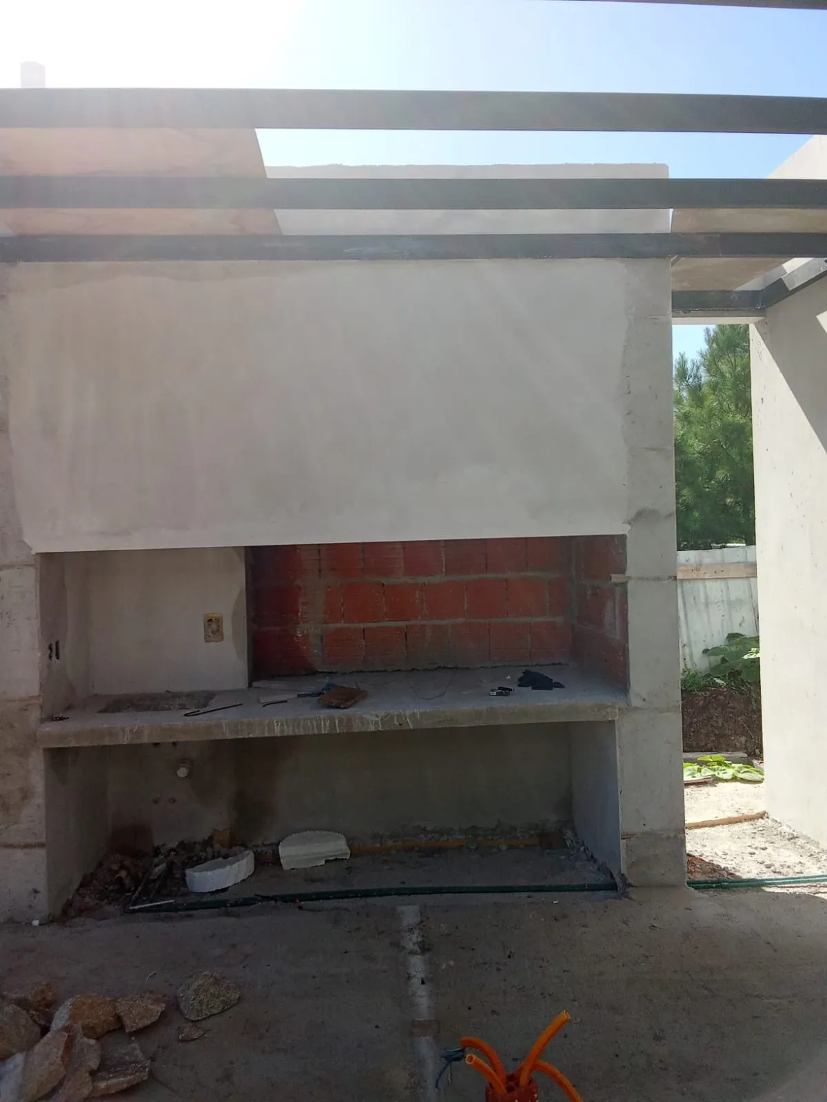 Barbacoa de obra con campana de hormigón bajo una pérgola, durante la construcción