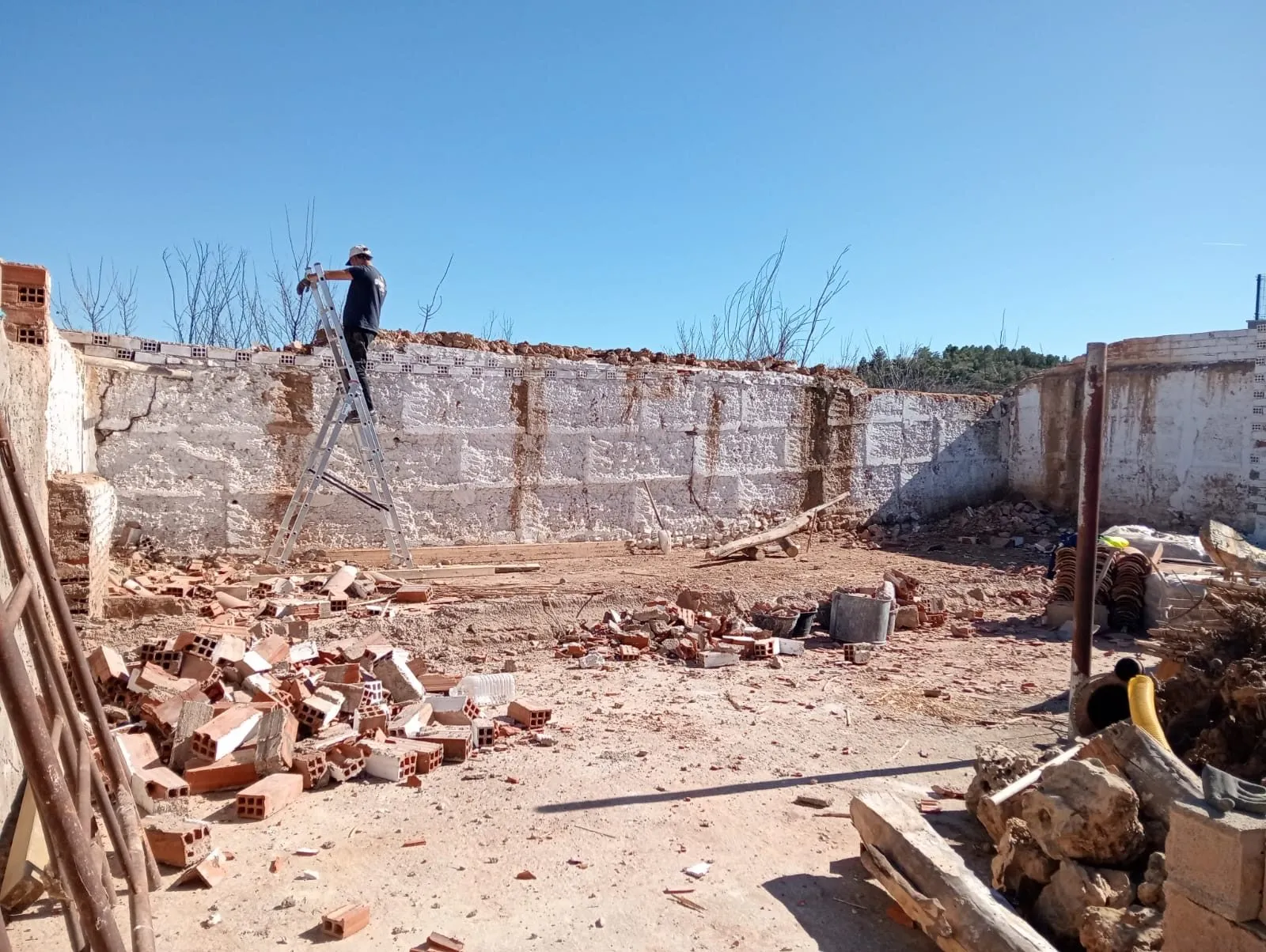 Muro de bloque en demolición con escombro y un operario en una escalera