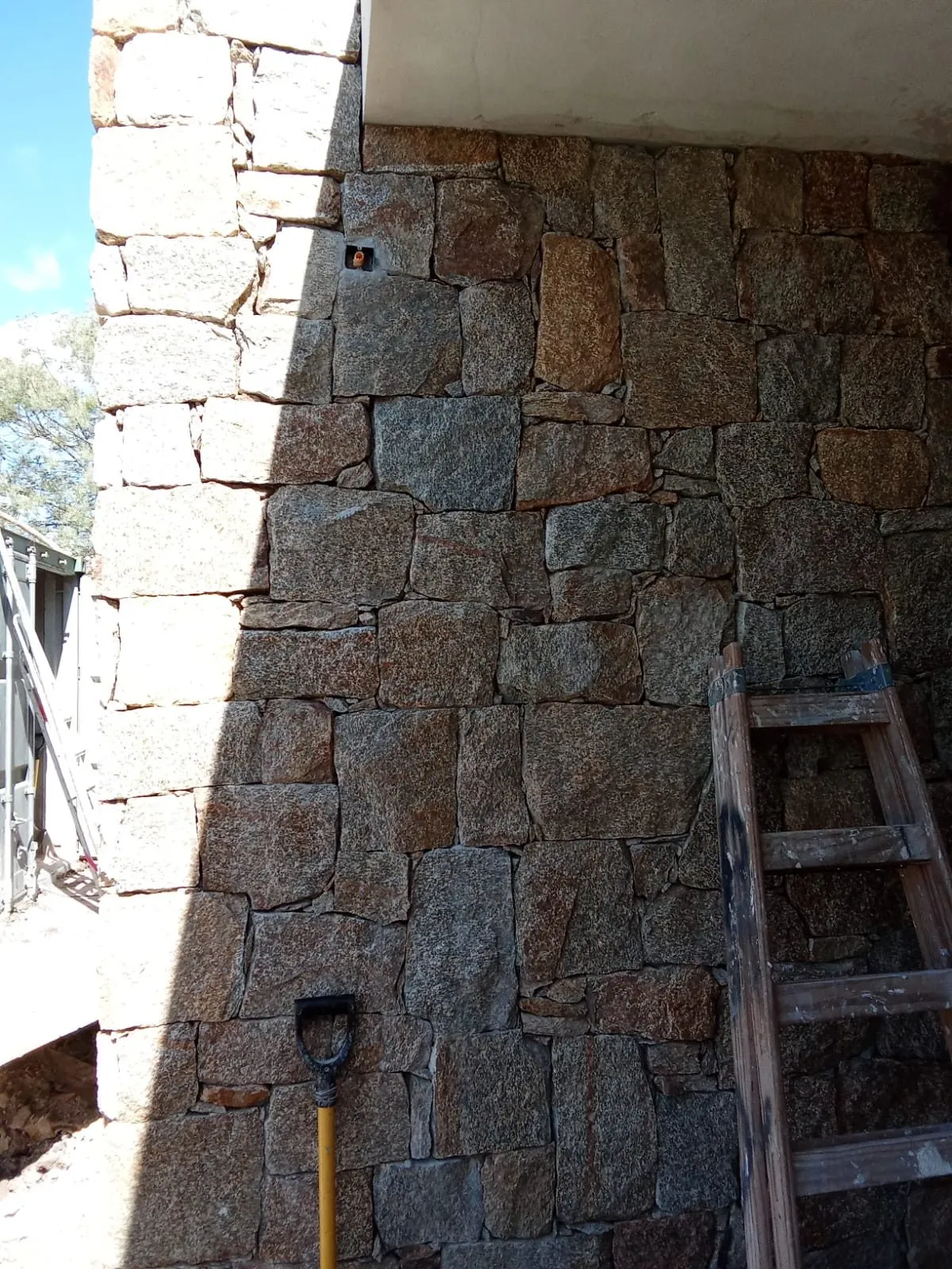 Muro de piedra natural en una zona cubierta, con una escalera apoyada