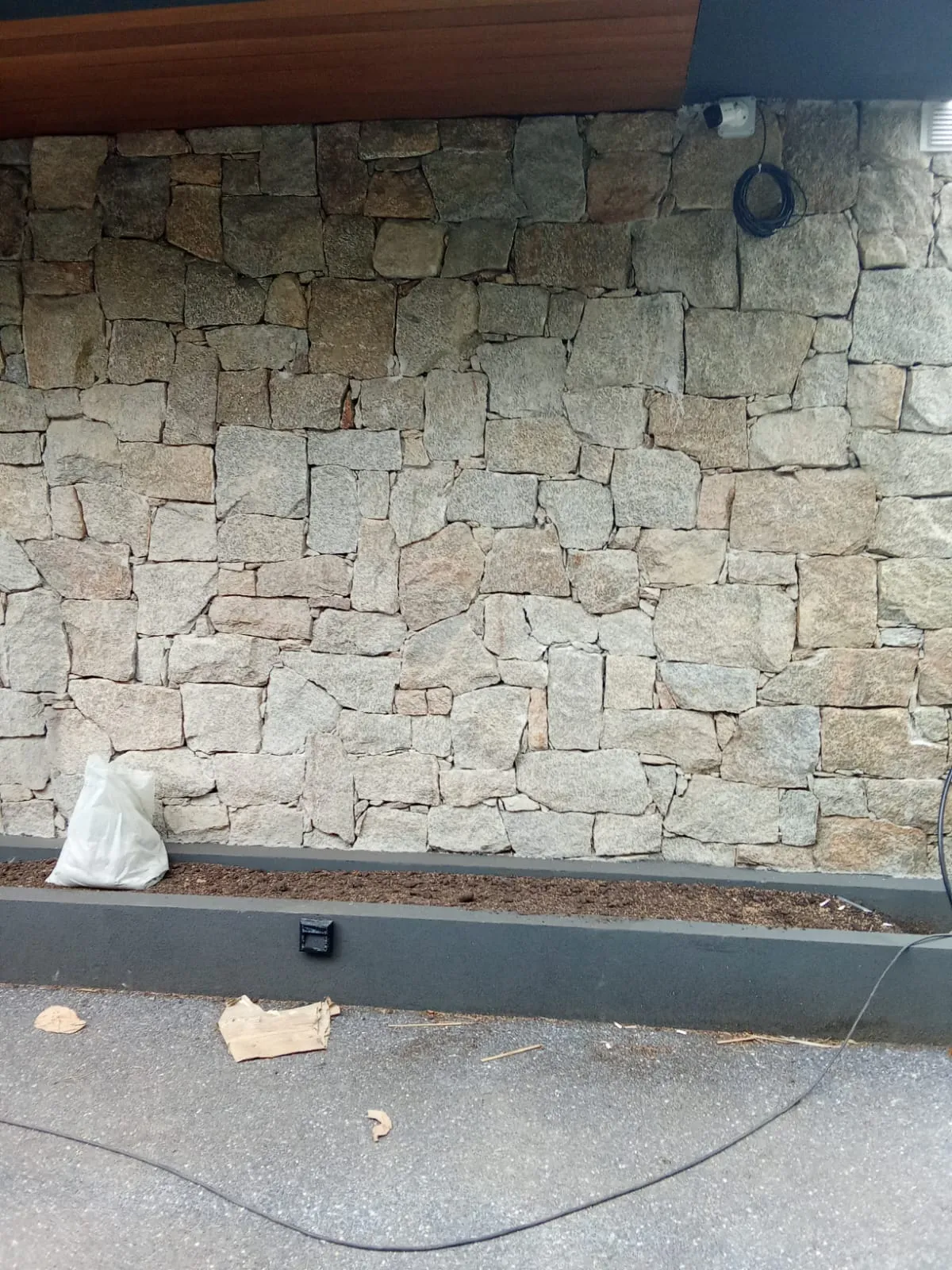 Muro de piedra natural con jardinera gris al pie