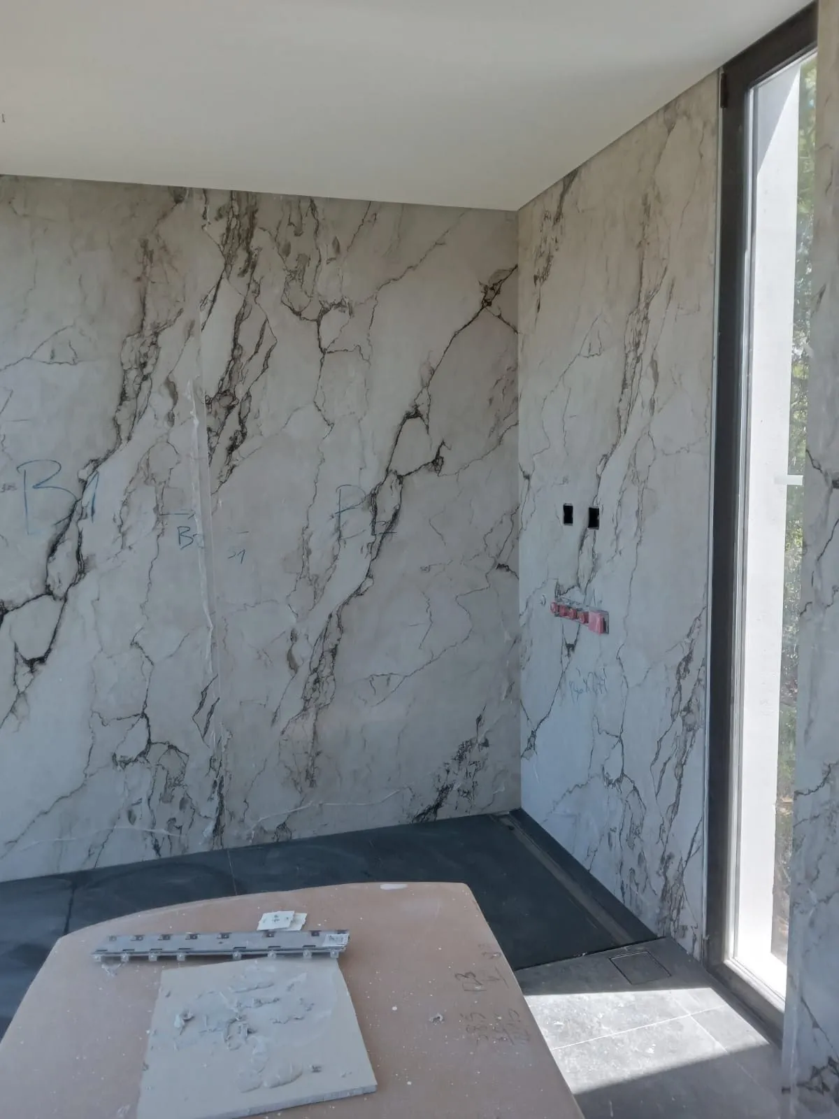 Esquina con pared de porcelánico efecto mármol y ventanal, durante la colocación