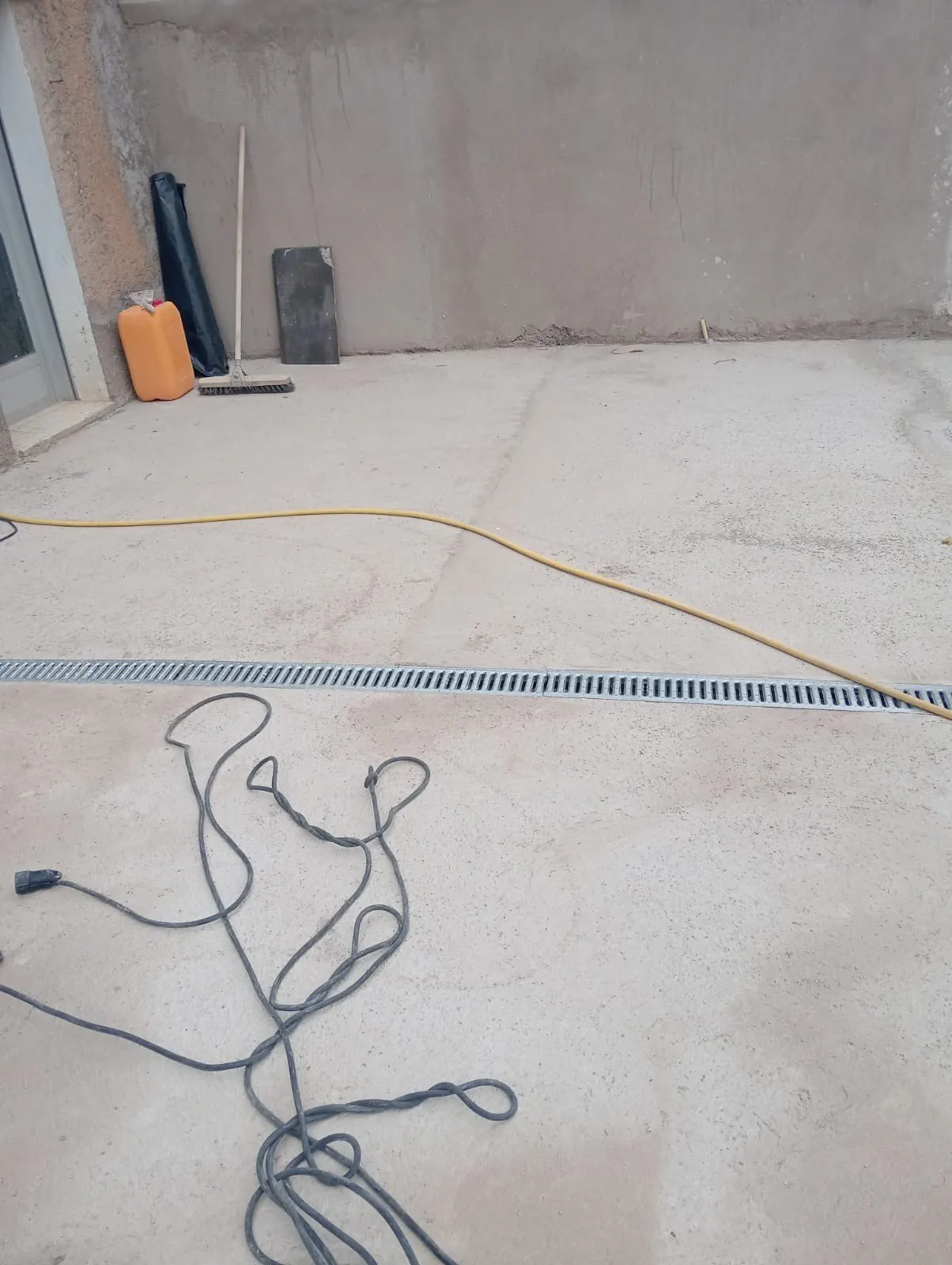 Solera de hormigón de un patio con un canal de drenaje de rejilla metálica junto al muro
