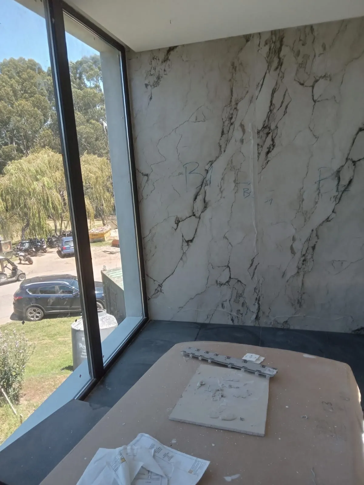 Pared de porcelánico efecto mármol junto a un gran ventanal, durante la obra